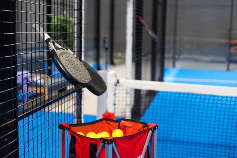 Paddle tennis: Padel racket and ball in front of an outdoor court.