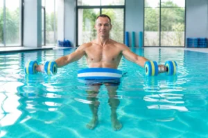 Adulte pratiquant un renforcement musculaire en piscine avec planche et haltères aquatiques dans une eau turquoise